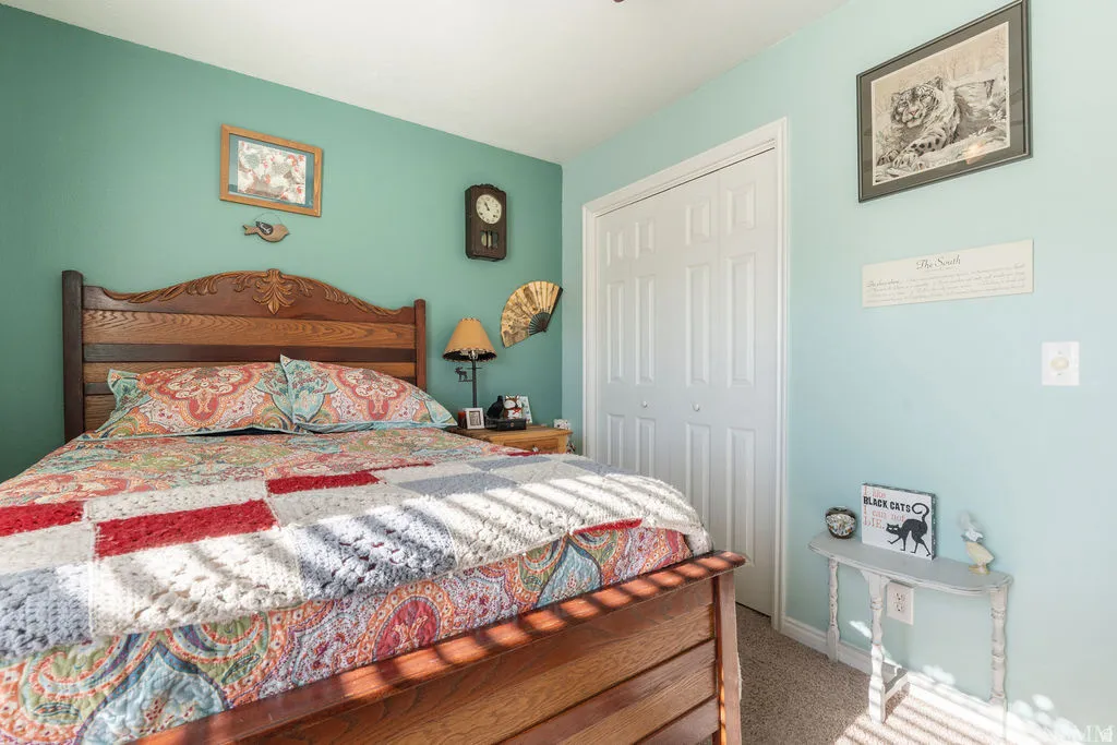 Carved wood headboard, paneled closet doors, wall-mounted clock, light-toned carpeting, and painted walls
