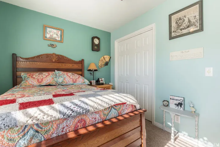 Carved wood headboard, paneled closet doors, wall-mounted clock, light-toned carpeting, and painted walls