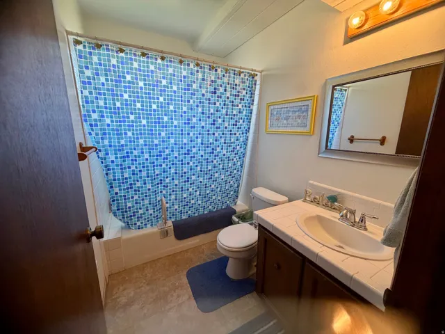 Spa-inspired bathroom featuring vibrant blue mosaic tile shower surround, white subway tile walls, ceramic pedestal sink with chrome fixtures, and neutral stone-finish flooring