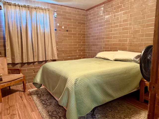 Comfortable bedroom showcasing exposed brick walls, wood-finish flooring, and a large window with natural light