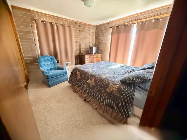 Spacious primary bedroom showcasing brick accent walls, dual windows with soft natural light, wood-finish flooring, and coordinating drapery