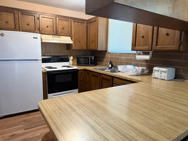 Spacious kitchen featuring wood-finish cabinetry, laminate countertops with extended island seating, black electric range, white refrigerator, and neutral tile backsplash
