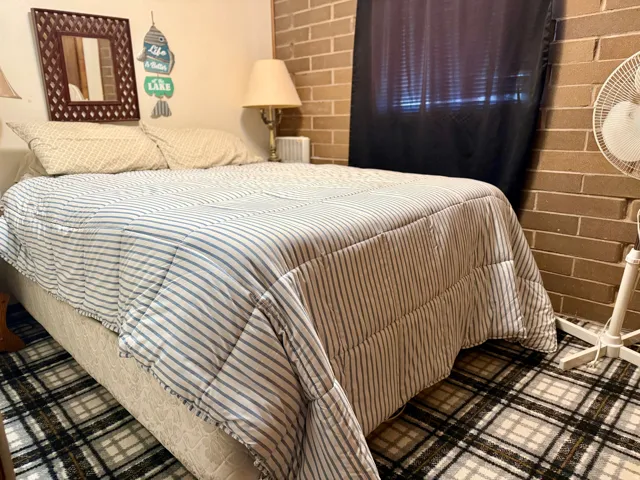 Brick accent wall with a dark window treatment, and plaid patterned carpet