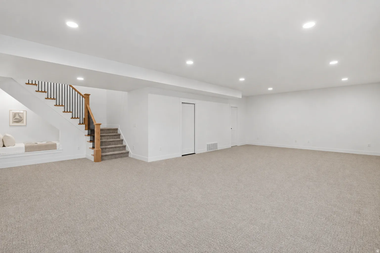 Expansive carpeted floor area with recessed lighting, a staircase featuring wood newel posts and handrail, black balusters, and a built-in window bench