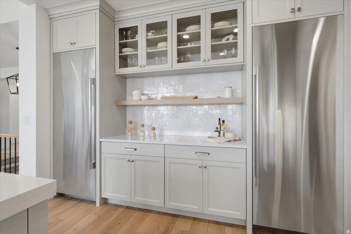 Stainless steel appliances, light wood-finish flooring, glass-front upper cabinetry, white subway tile backsplash, and light-toned countertops