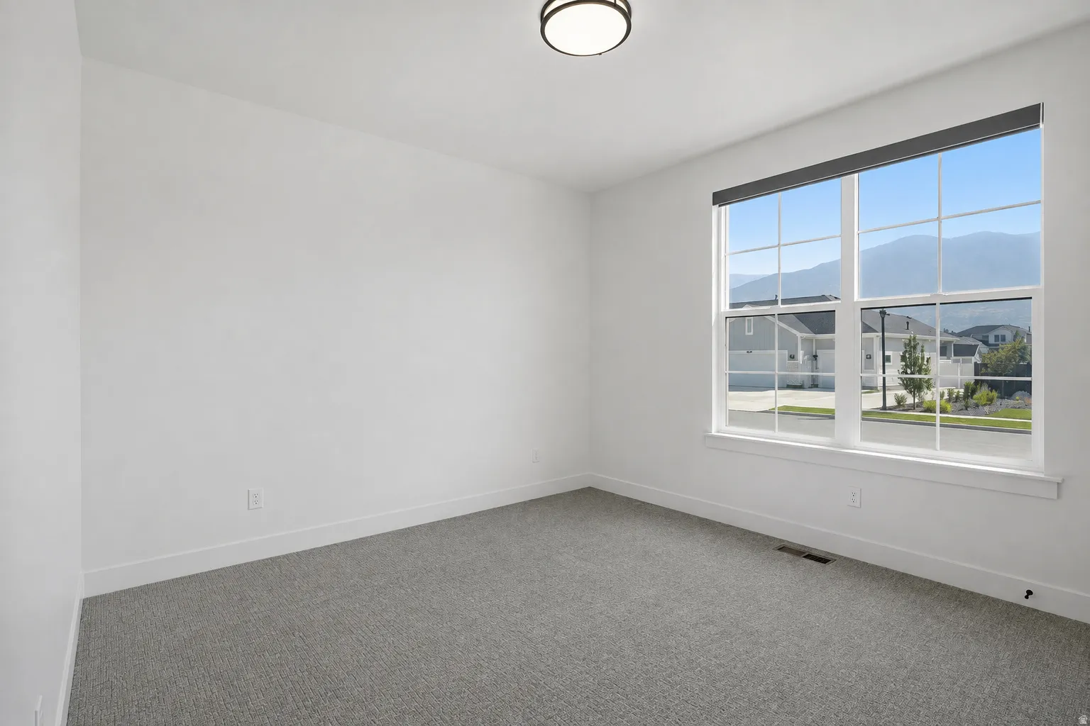 Spacious room with large window, white trim, grey carpeting, and a flush mount ceiling light