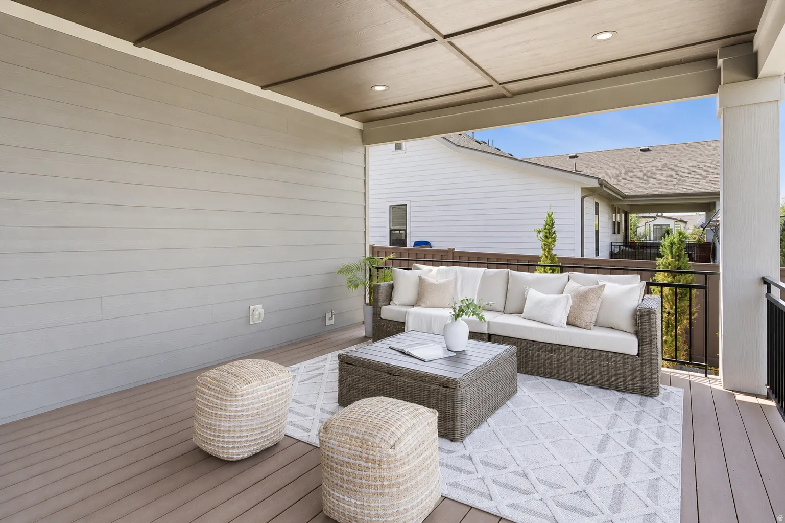 Expansive covered patio featuring a slatted ceiling with recessed lighting, composite decking, and a black metal railing