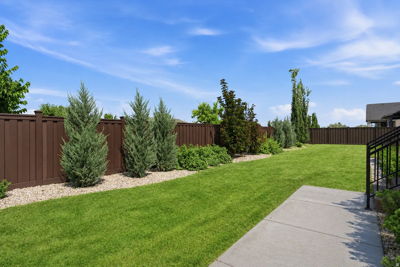 Expansive backyard featuring a manicured lawn, established landscaping, privacy fencing, and a concrete patio with railings