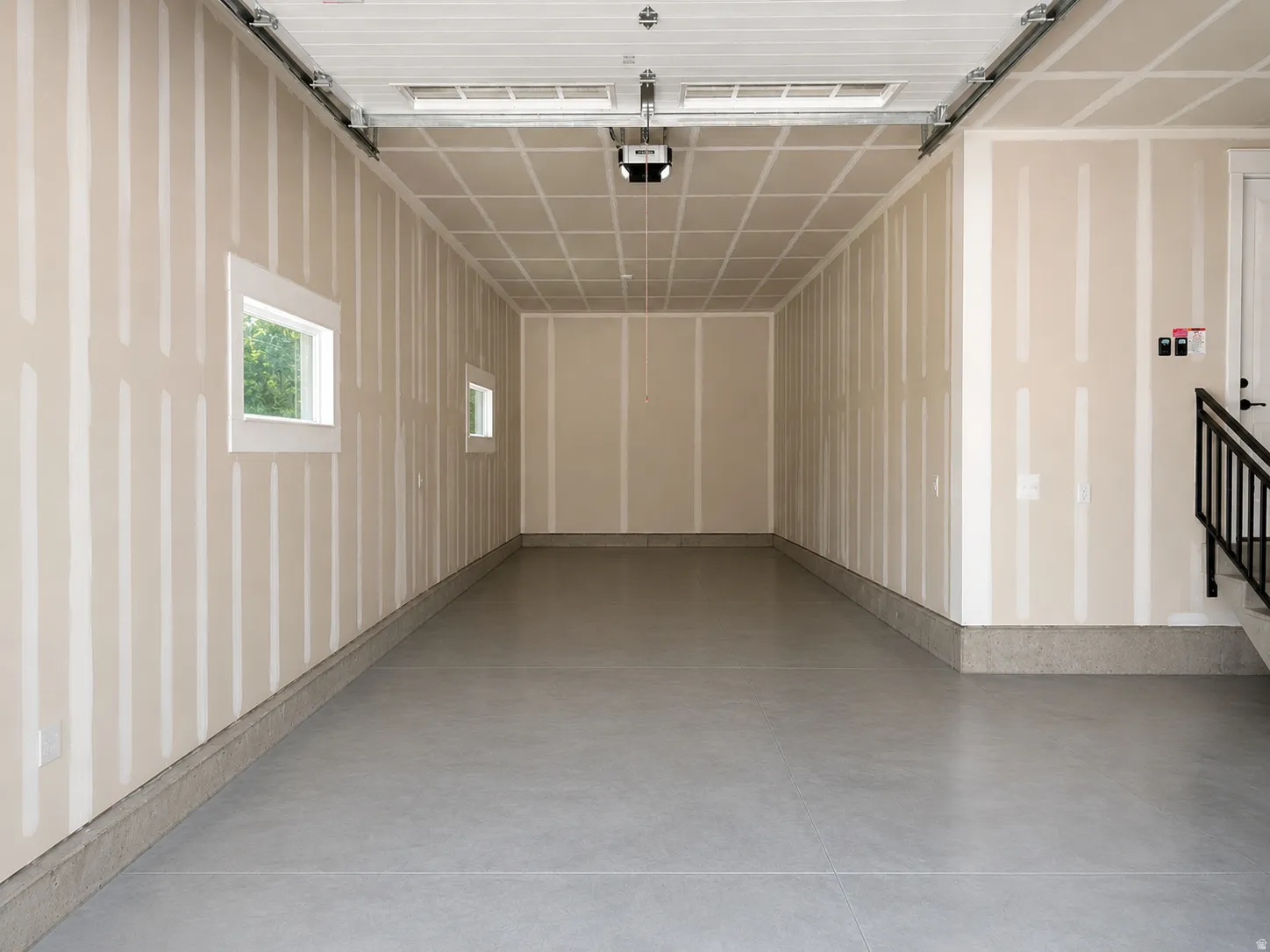 Expansive garage space with concrete flooring, two windows, and a built-in stairwell with railing