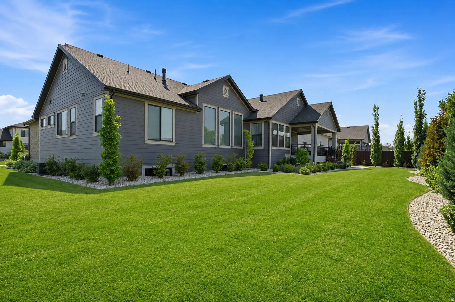 Spacious lawn area with established landscaping, featuring an exterior with dark siding and multiple large windows