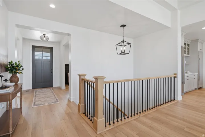 Light wood-finish flooring throughout, a dark paneled entry door with glass inserts, and a staircase featuring light wood newel posts and black metal balusters