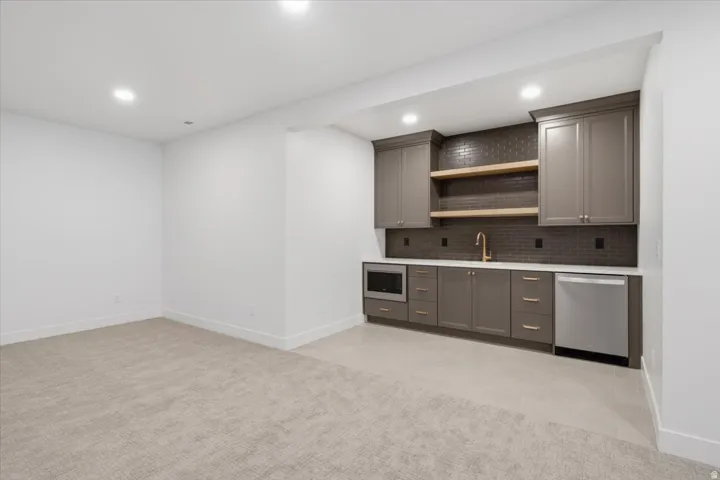 Built-in wet bar with wood-finish open shelving, gray cabinetry, and a stainless steel undercounter refrigerator