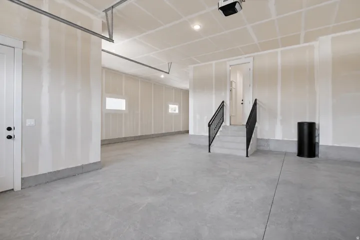 Concrete flooring, overhead garage door system, interior access door, stairwell with black metal handrails, and transom windows