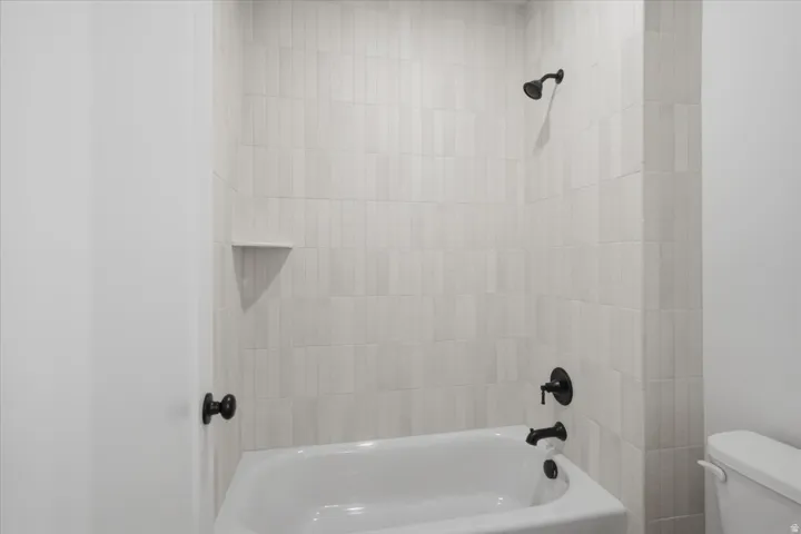 Bathtub with matte black fixtures, tiled surround, and integrated corner shelf