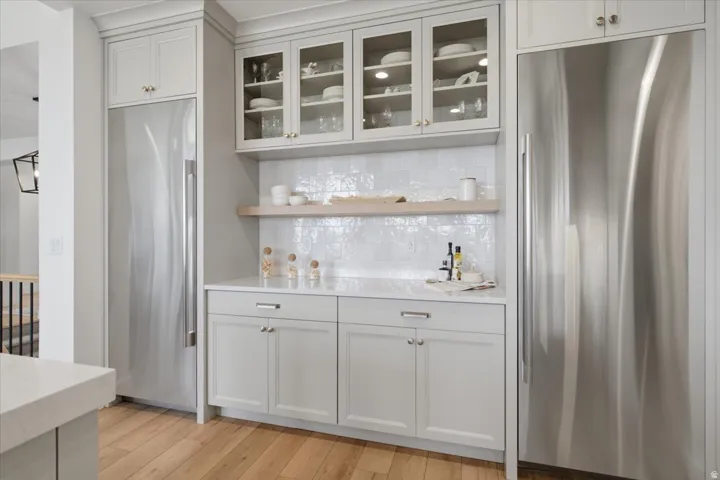 Stainless steel appliances, light wood-finish flooring, glass-front upper cabinetry, white subway tile backsplash, and light-toned countertops