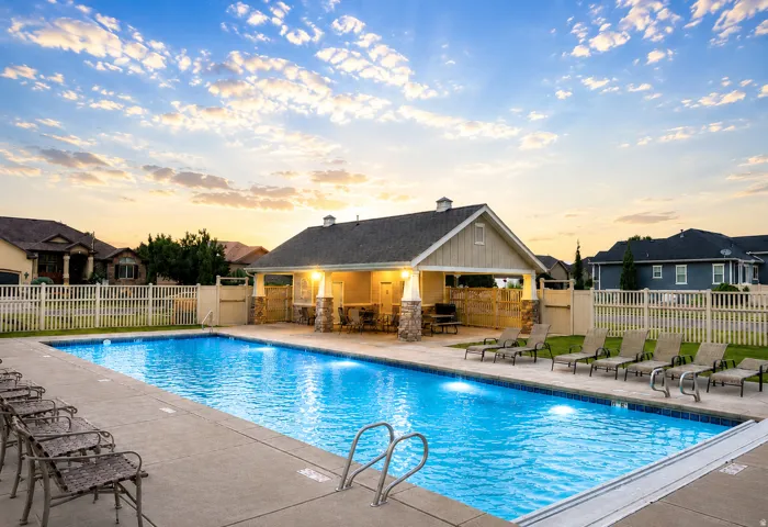 Outdoor swimming pool with integrated lighting, a concrete surround, and a coordinating pool house featuring stone-clad columns and an attached covered patio