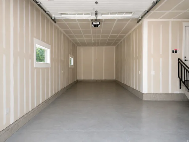 Expansive garage space with concrete flooring, two windows, and a built-in stairwell with railing