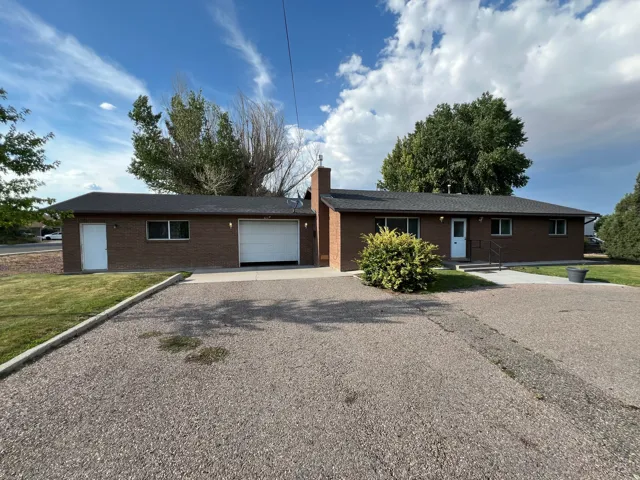 Brick ranch home featuring a spacious asphalt driveway, two-car garage, and mature landscaping with established trees