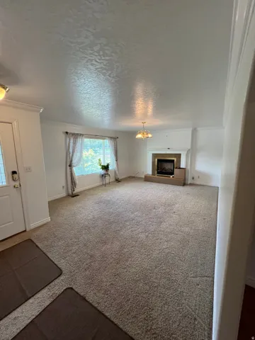 Spacious living area featuring a corner fireplace with a mantel, broad window, and a chandelier
