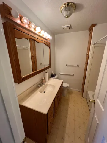 Bathroom features a wood-finish vanity with an integrated sink and countertop, tri-bulb vanity lighting, and ceramic tile flooring