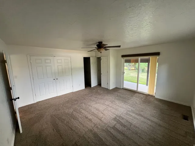 Spacious room featuring carpeting, a ceiling fan, sliding glass doors, and dual bi-fold closet doors