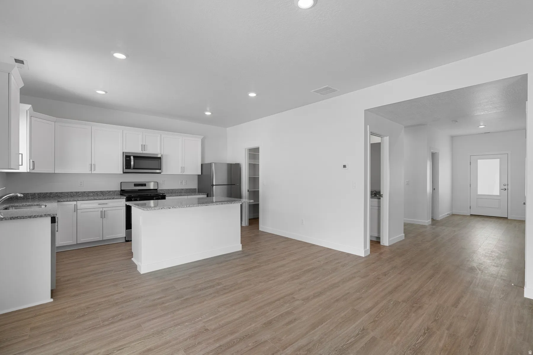 Open-concept kitchen featuring white cabinetry, stainless steel appliances, granite countertops, and wood-finish flooring