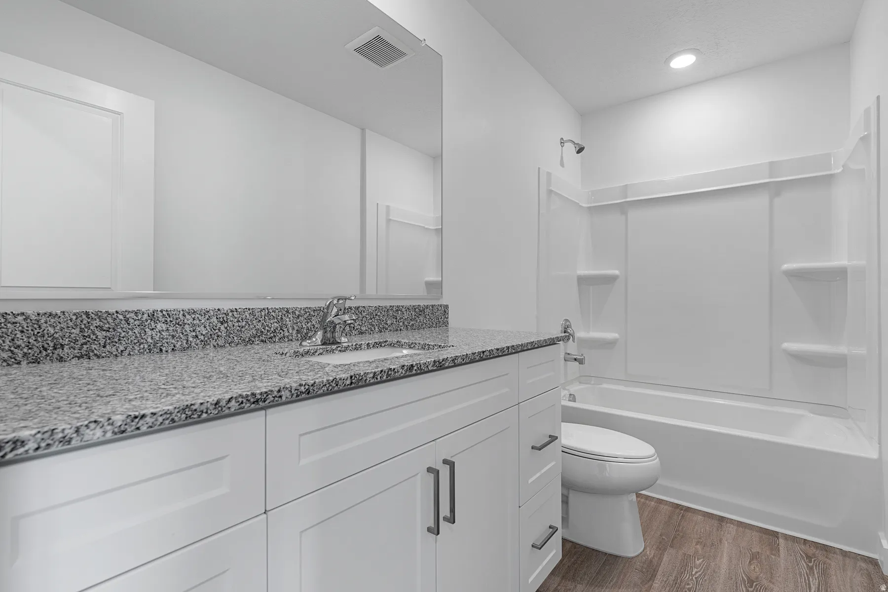 Bathroom featuring a white vanity with an undermount sink, granite countertop, a bathtub with a shower, and wood-finish flooring