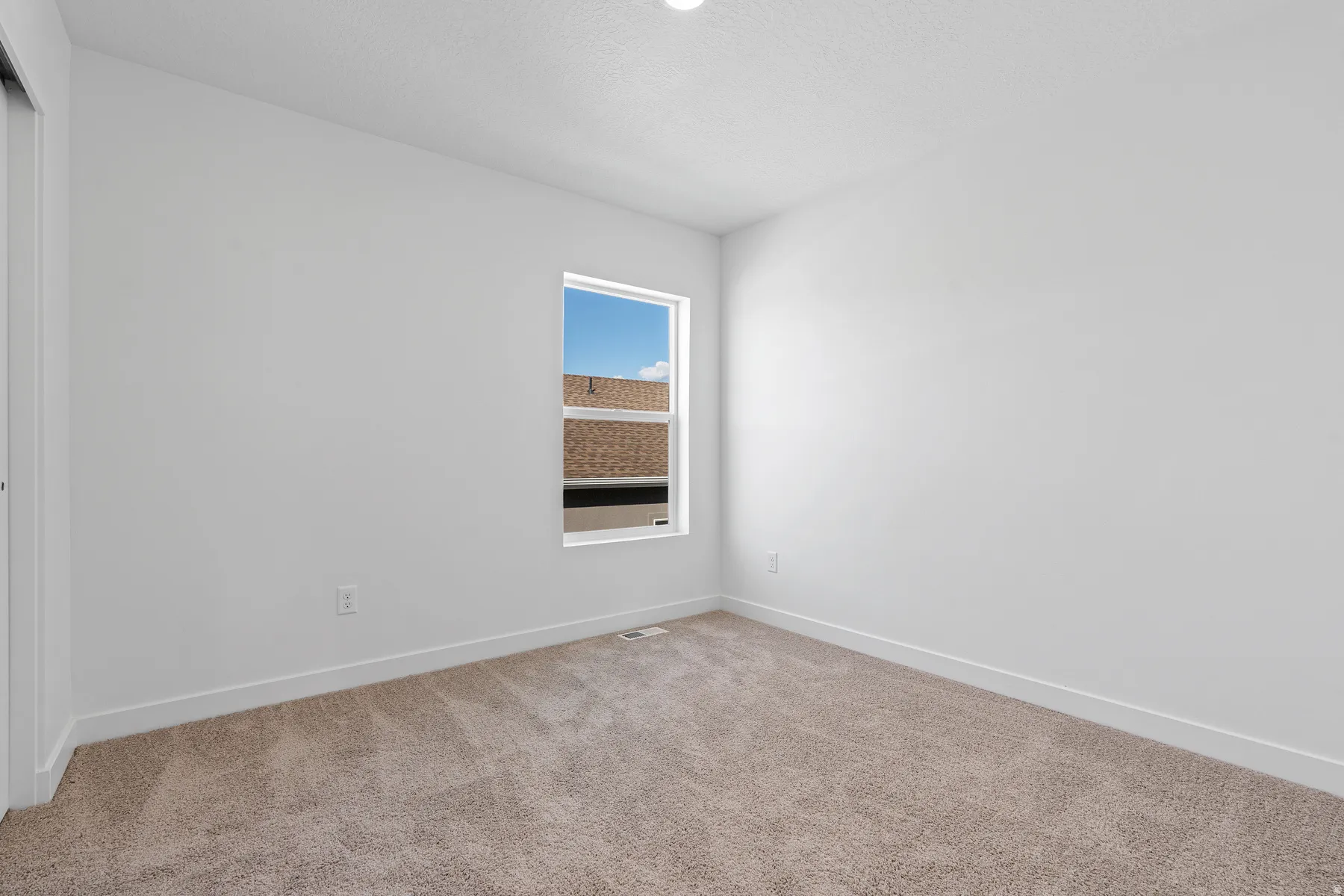 Neutral wall paint, plush carpet flooring, and a single window with a white frame