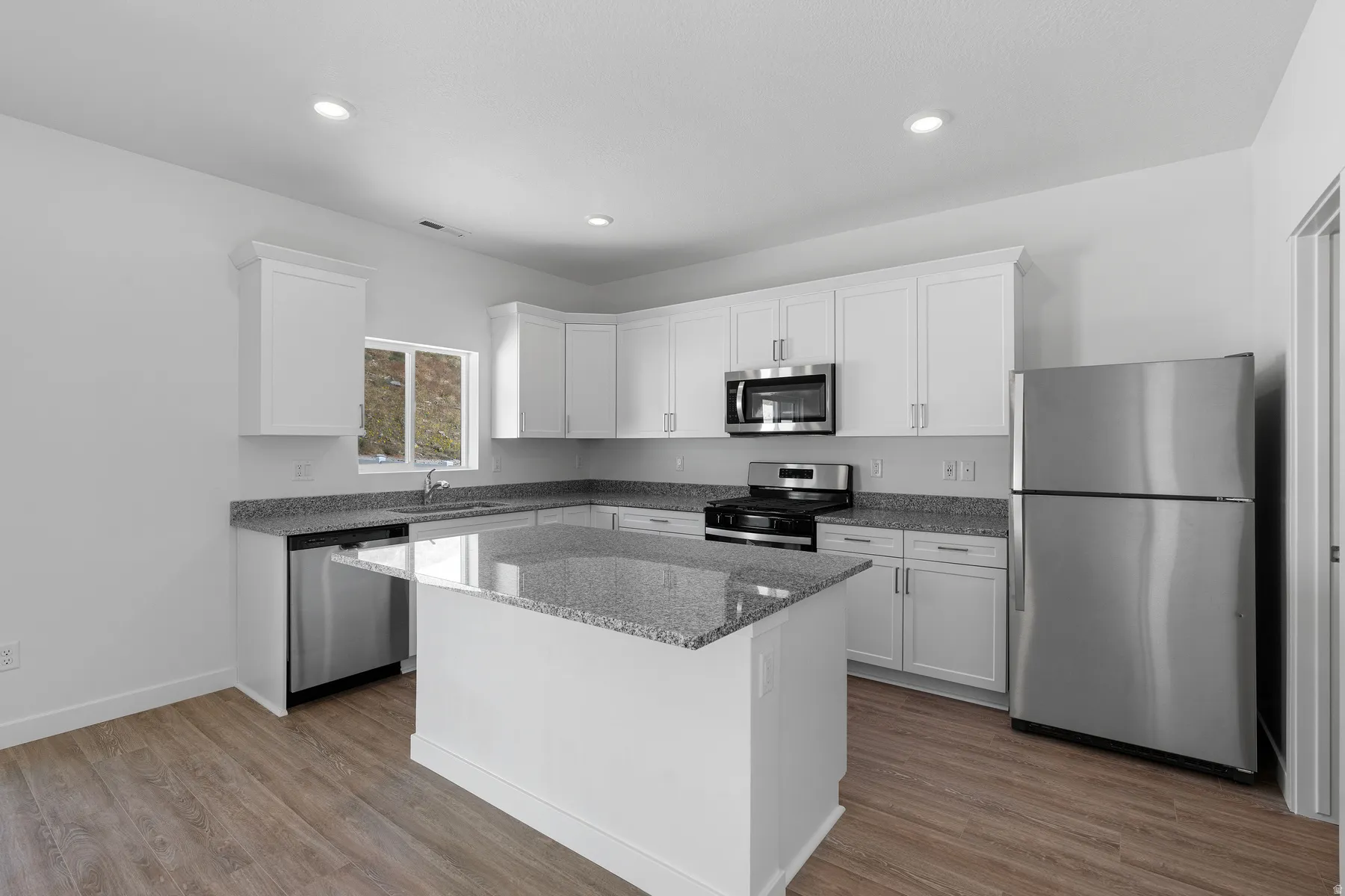 Modern kitchen featuring white cabinetry, stainless steel appliances including a built-in microwave and refrigerator, gray quartz countertops, a centered island with additional counter space, wood-finish flooring, and recessed ceiling lighting