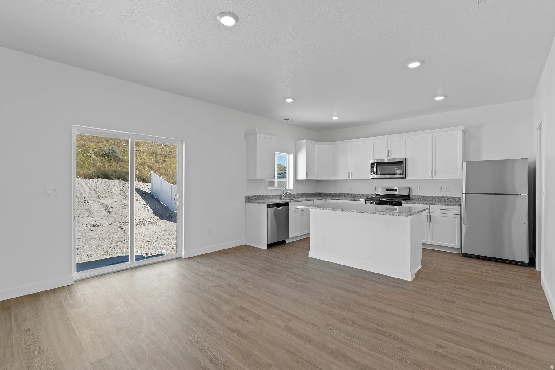 Modern kitchen featuring white cabinetry, stainless steel appliances including a gas cooktop and microwave, a centered island with seating space, quartz countertops, and wood-finish flooring throughout