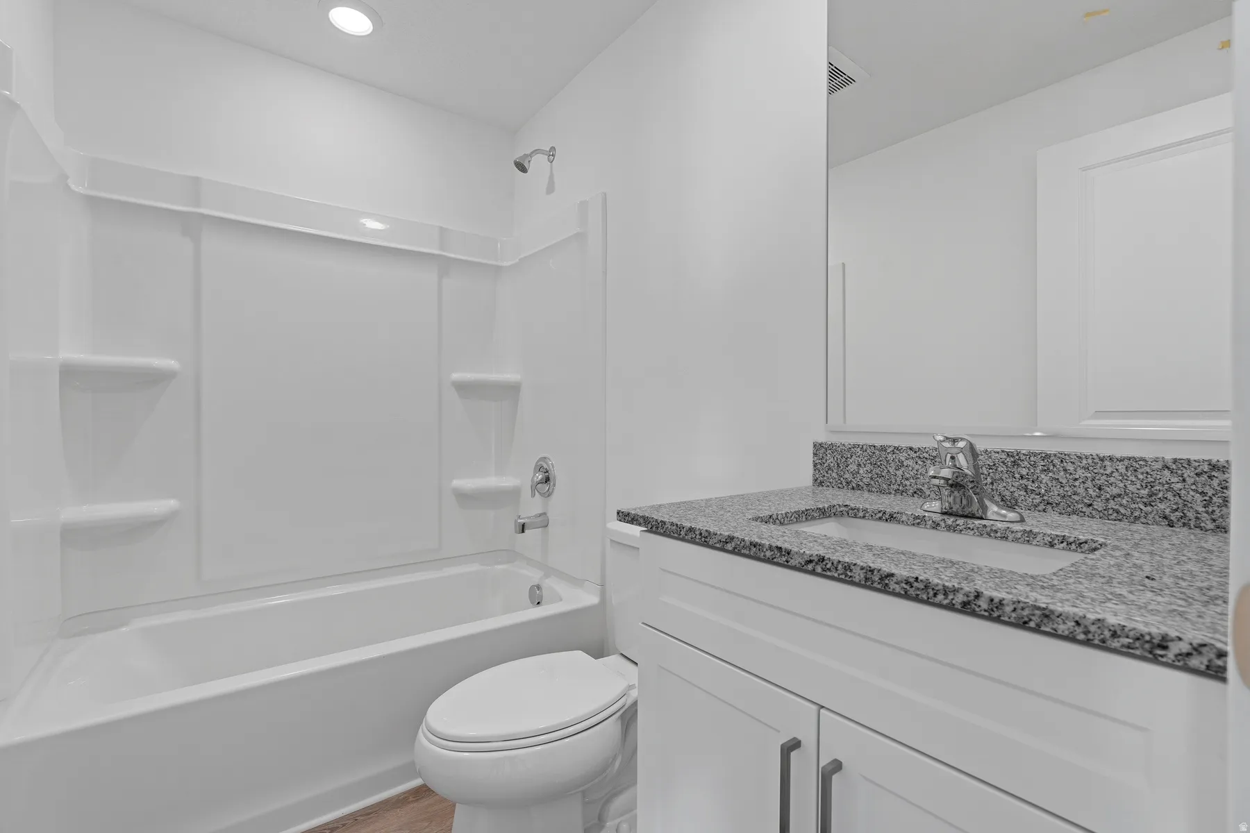 Modern bathroom featuring a granite-topped vanity with dual undermount sink, white cabinetry with brushed metal hardware, and a subway tile shower surround with recessed shelving
