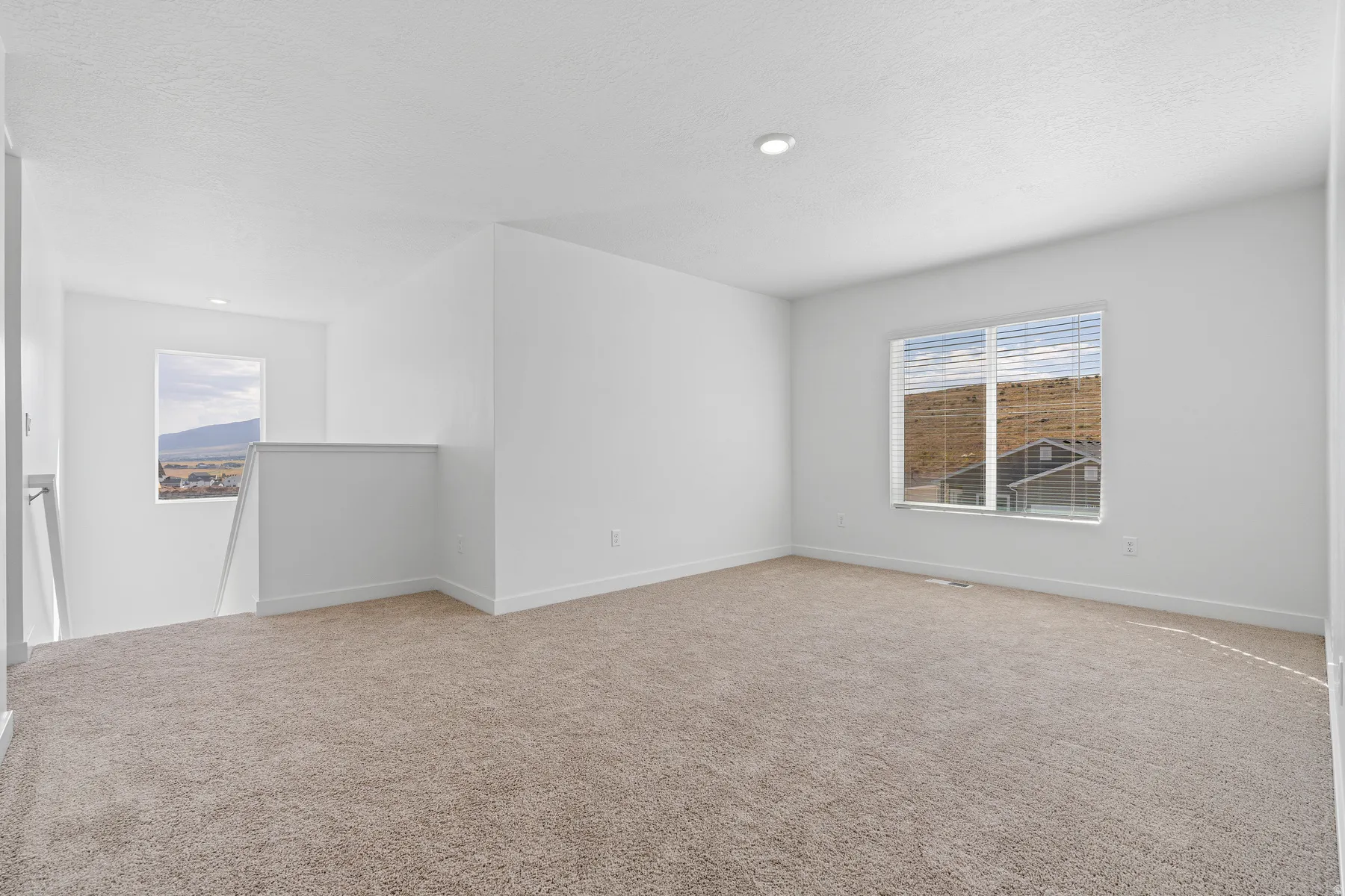 Bright, open living space featuring neutral carpeting, recessed ceiling lighting, and abundant natural light from large dual-pane windows
