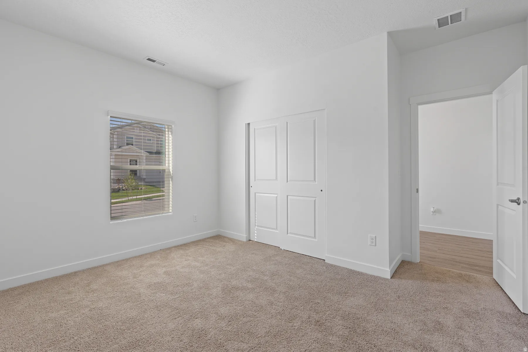 Neutral-toned carpet flooring, white walls, and a window with horizontal blinds