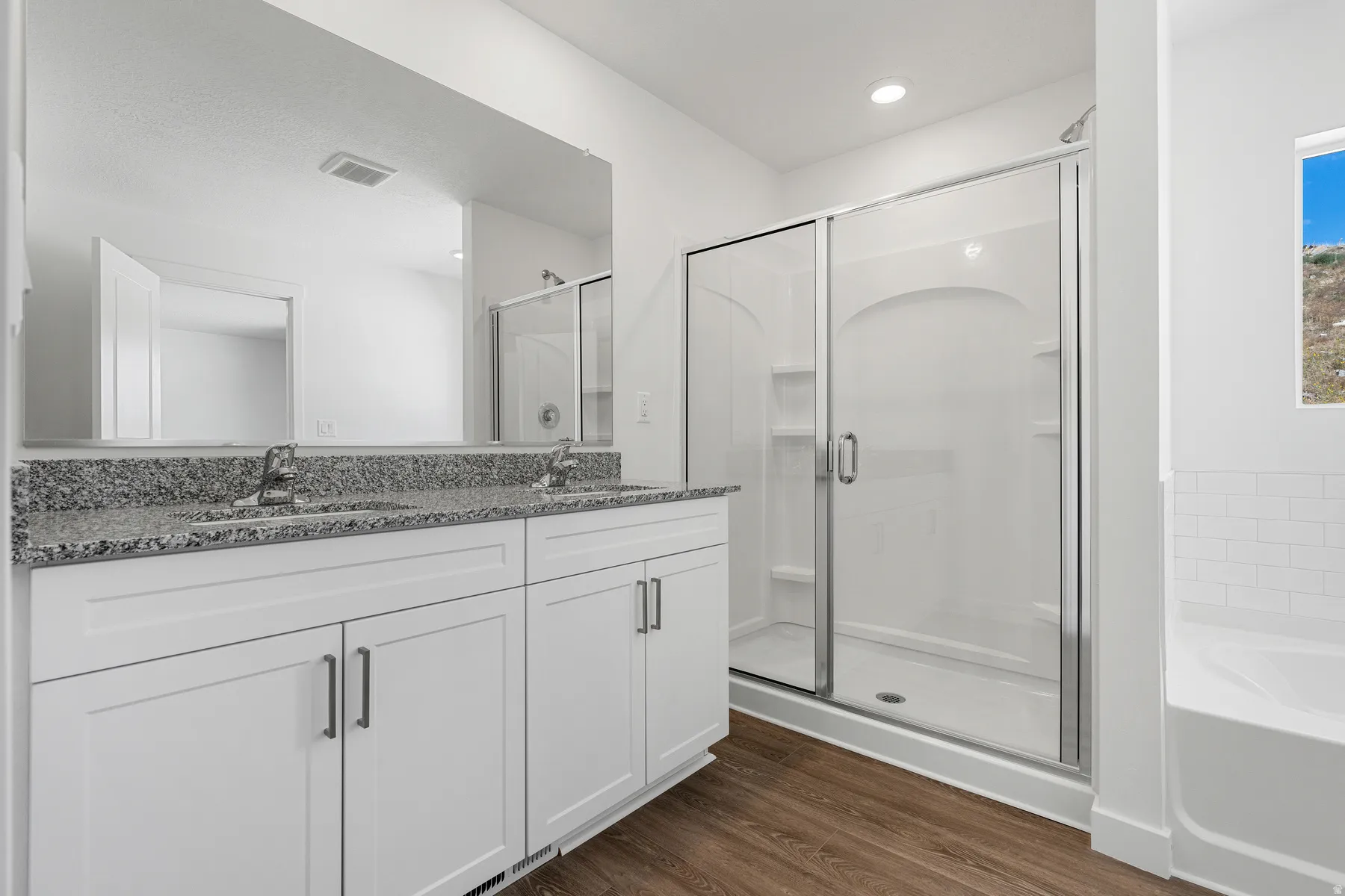 Dual vanity with granite countertop, wood-finish flooring, glass-enclosed shower, built-in bathtub, and window with natural light