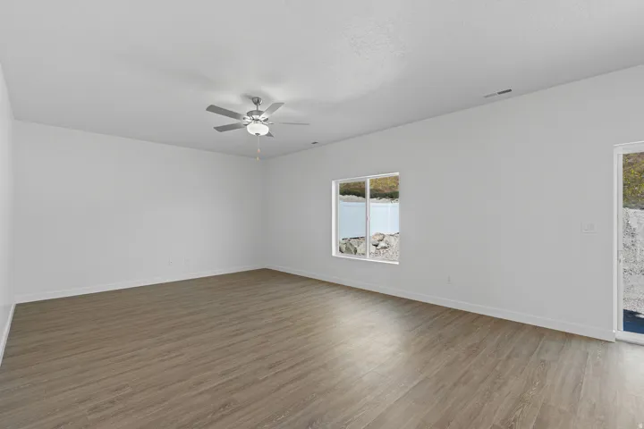 Spacious room featuring wood-finish flooring, white walls, a ceiling fan with integrated lighting, and a large window with a water and landscape backdrop