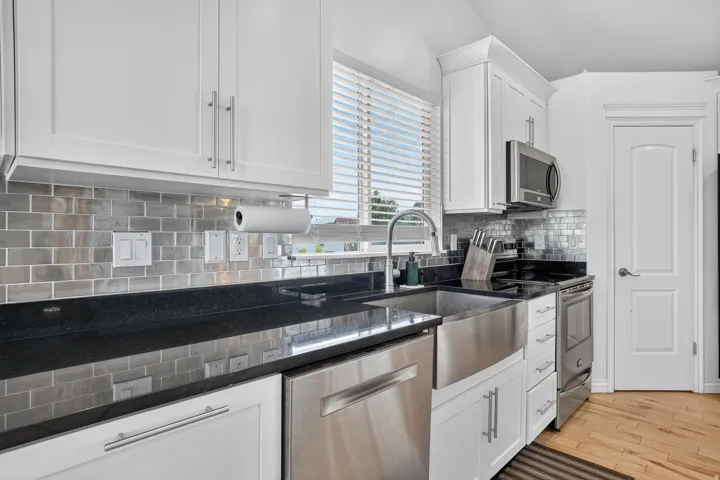 White cabinetry with brushed nickel hardware, dark countertops, a stainless steel apron front sink, subway tile backsplash, and wood-finish flooring