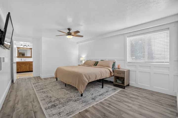 Wood-finish flooring, ceiling fan with integrated lighting, window with blinds, and white panel wall detailing