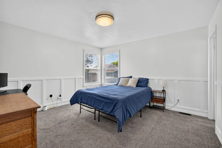 White interior walls with wainscoting, light gray carpet flooring, two windows with blinds, and a flush mount ceiling light