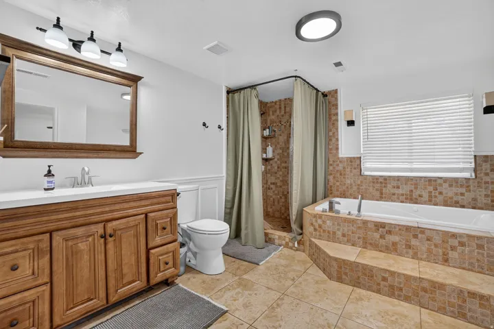 Bathroom featuring a wood-finish vanity with a white countertop, an integrated shower with tile surround, a built-in bathtub with a tiled deck, and light-colored floor tiling