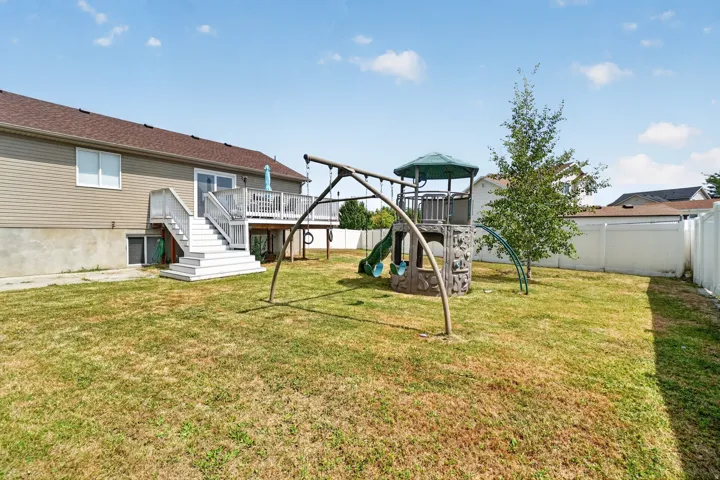 Expansive backyard featuring a multi-level deck with stairs, vinyl siding, a privacy fence, and a mature tree