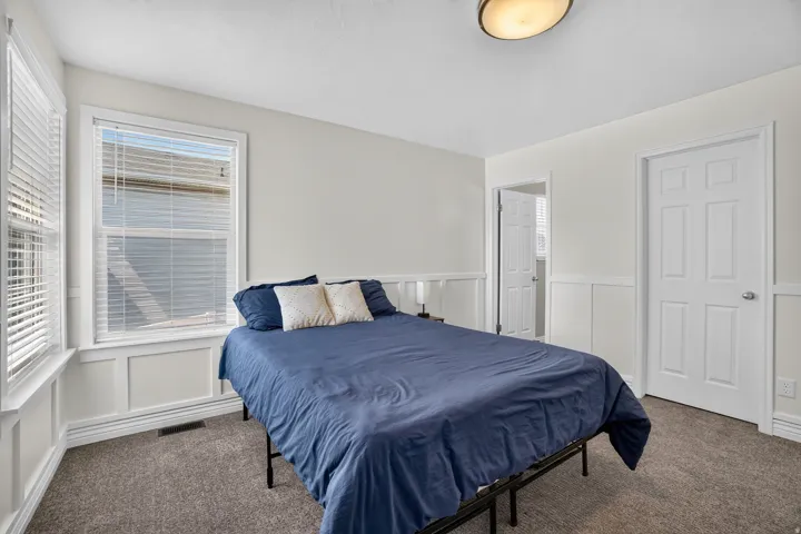 Neutral wall colors, white paneled wainscoting, two windows with blinds, two paneled doors, and a flush mount ceiling light