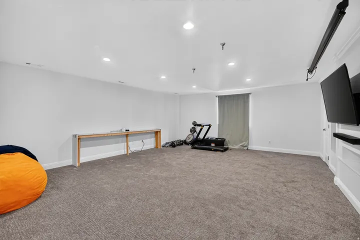 Recessed lighting, light gray wall finishes, gray carpet, window with light gray drapery, and a wall-mounted entertainment unit