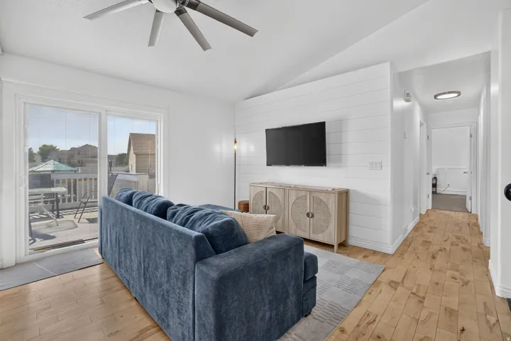 Vaulted ceiling with a ceiling fan, white shiplap accent wall, wood-finish flooring, and a sliding glass door opening to an outdoor deck