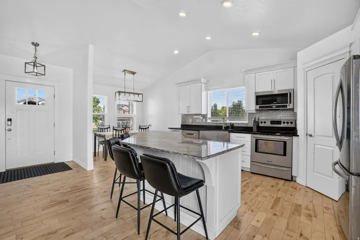 Light wood-finish flooring throughout, kitchen island with granite countertop, stainless steel appliances, white cabinetry, and recessed lighting