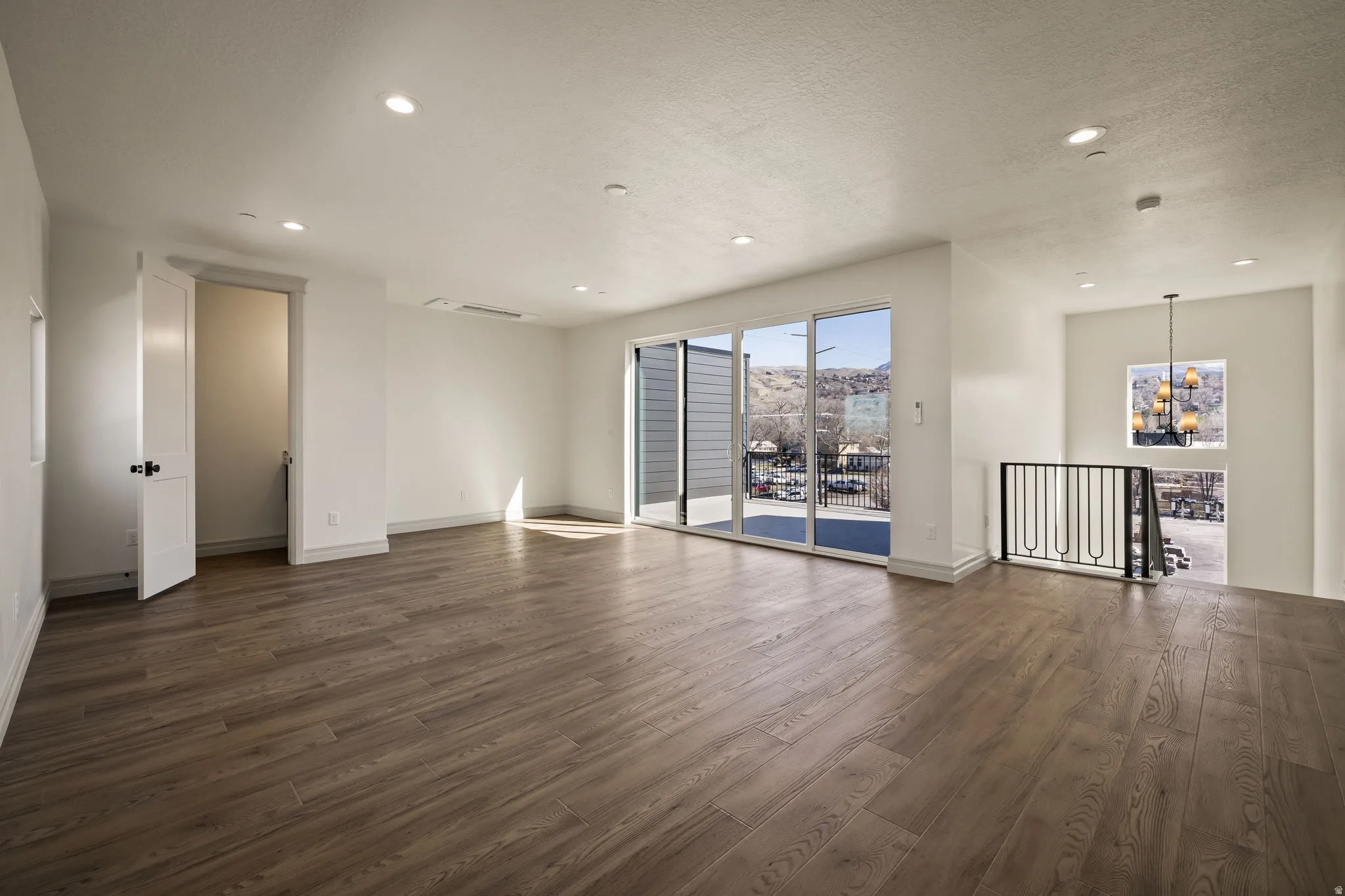 Spacious open-concept living area featuring wide-plank wood-finish flooring, recessed ceiling lighting, and expansive glass sliding doors with panoramic cityscape views