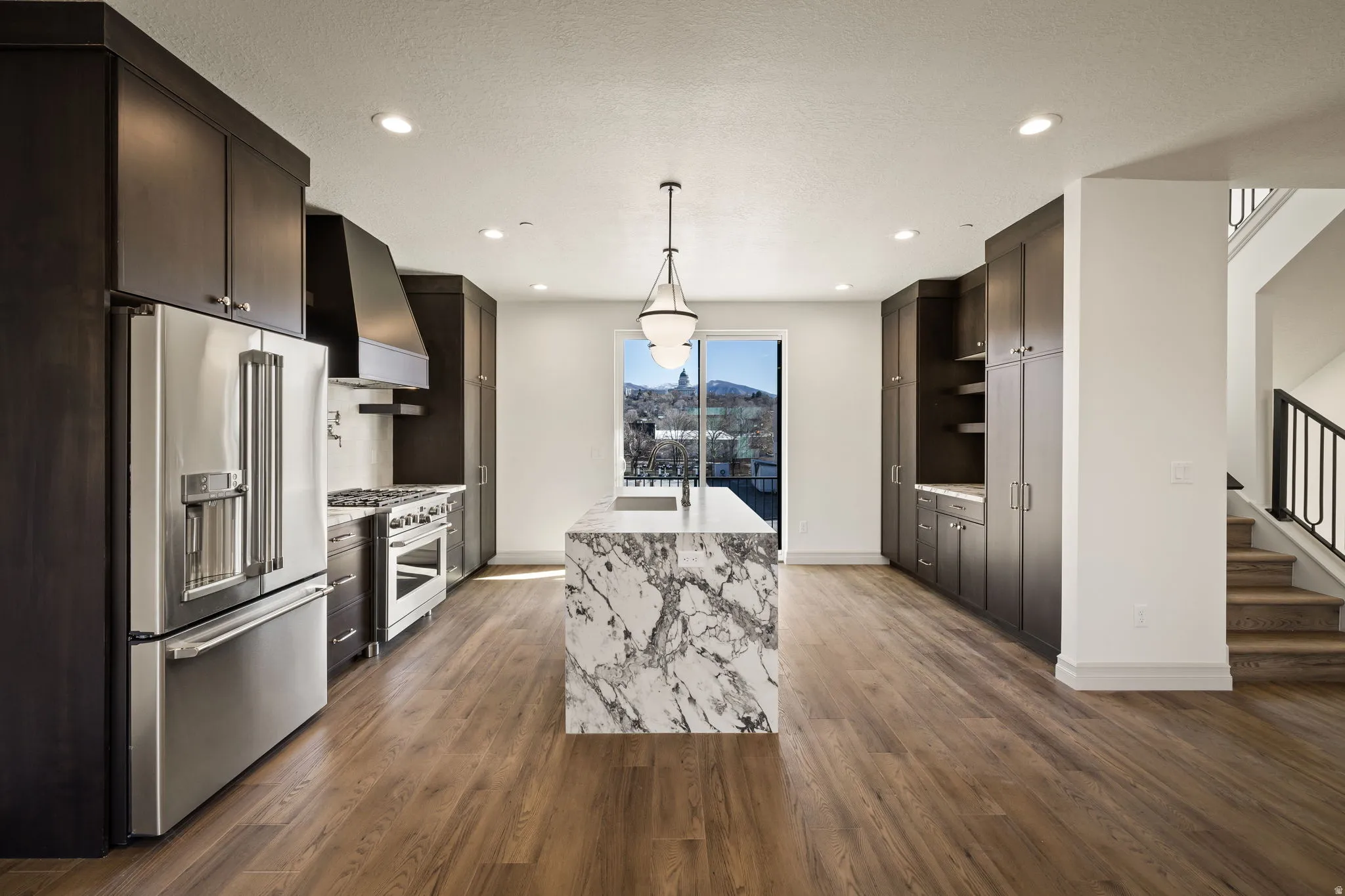 Gourmet kitchen featuring a waterfall island, stainless steel appliances, dark wood-finish cabinetry, wood-finish flooring, and a contemporary pendant light fixture