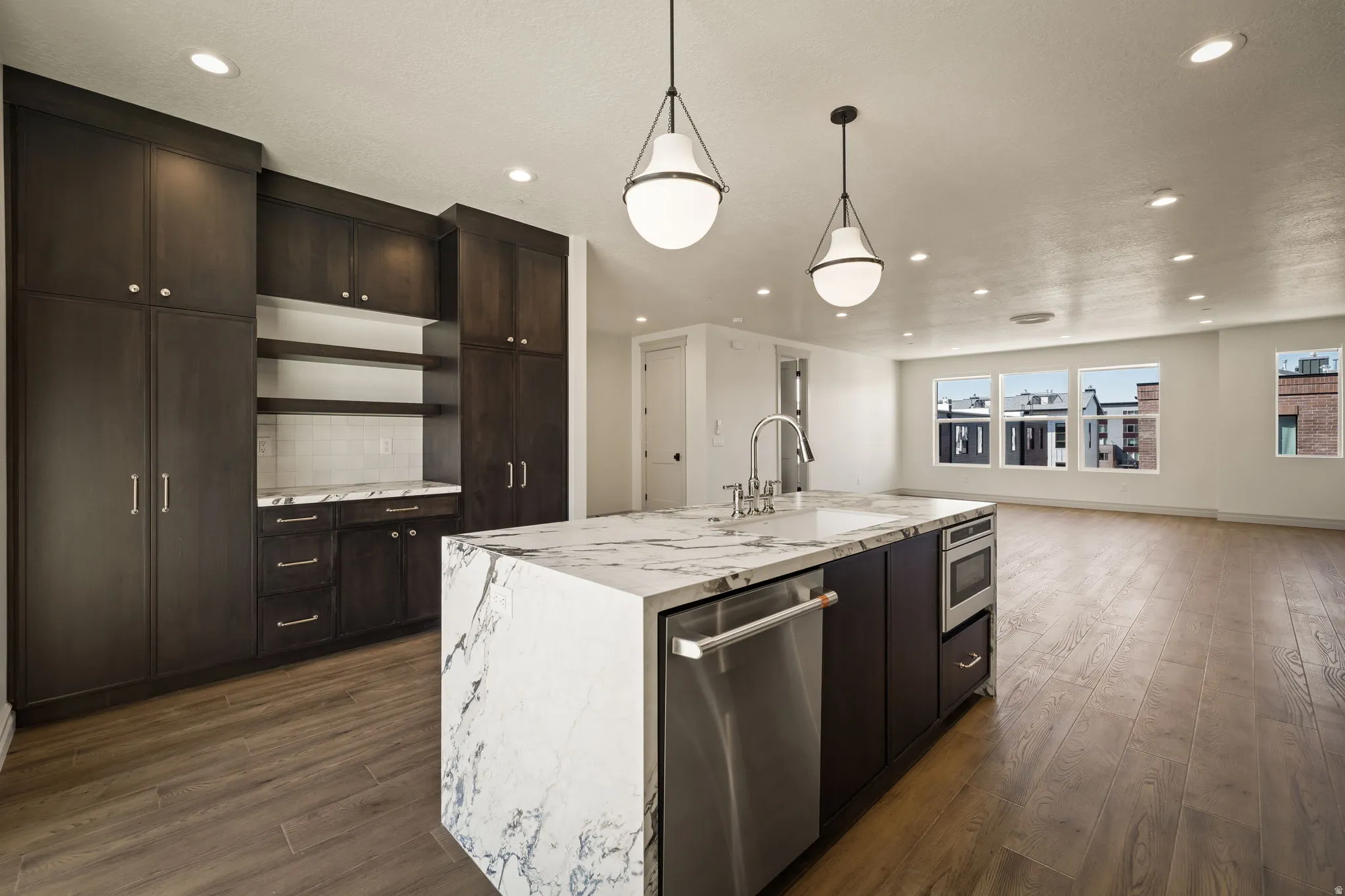 Sophisticated open-concept kitchen featuring a large island with white stone-look countertops and black cabinetry, stainless steel appliances, pendant lighting, dark wood-finish flooring, and abundant natural light from multiple windows