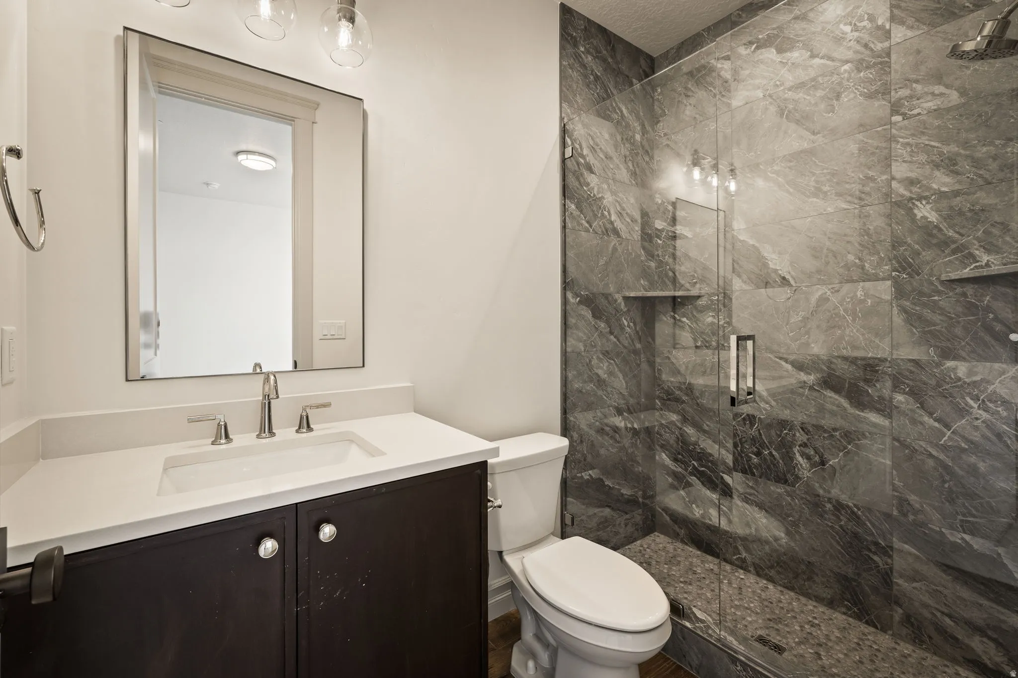 Contemporary bathroom featuring a dark vanity with dual-sink configuration, white quartz countertop, framed mirror with integrated lighting, and polished chrome fixtures