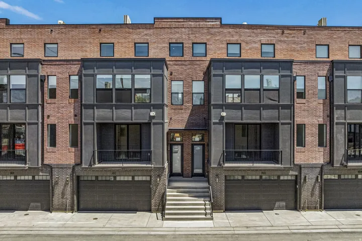 Contemporary brick townhome featuring a symmetrical facade with large multi-pane windows, modern dark-framed glass entries, and integrated two-car garage bays with dark paneling