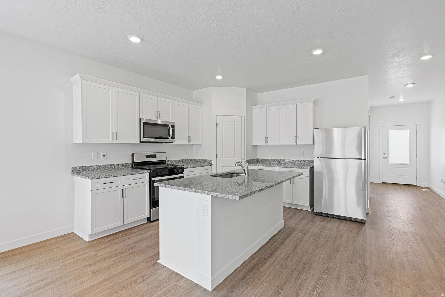 Modern kitchen featuring white cabinetry, stainless steel appliances including a microwave and refrigerator, gray quartz countertops, a center island with additional storage, recessed lighting, and wood-finish flooring throughout the open layout